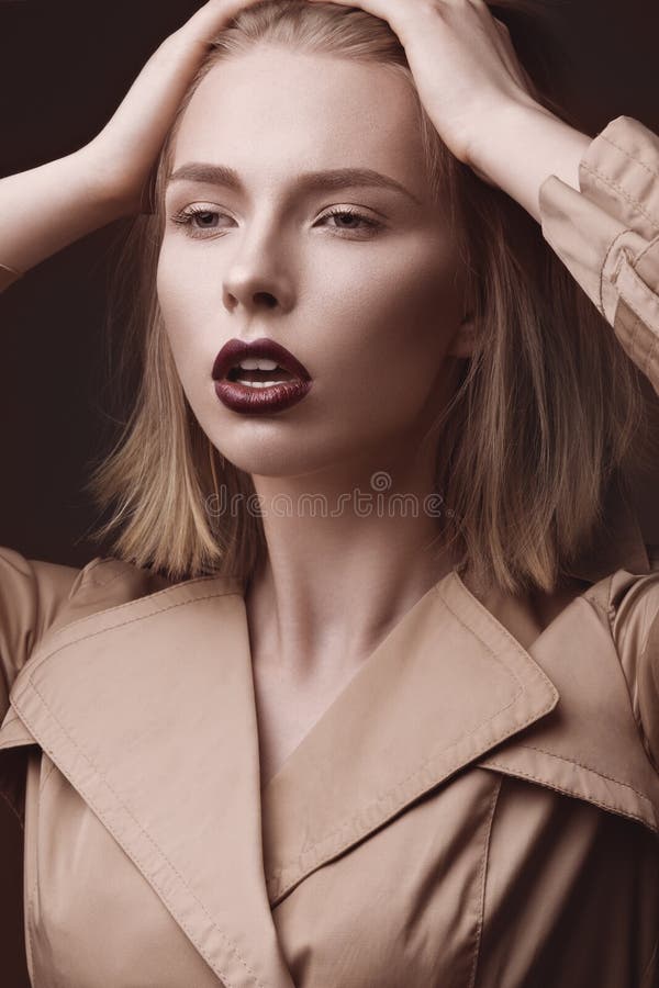 Belle femme blonde dans un manteau lumineux et des lèvres foncées, montrant différentes poses Visage de beauté image stock Belle femme blonde dans un manteau lumineux et des lèvres foncées, montrant différentes poses Visage de beauté image stock