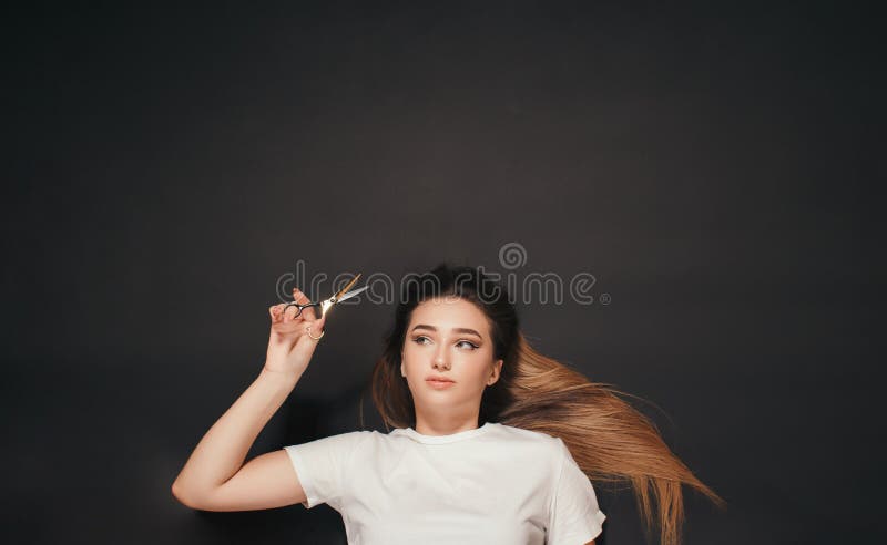 Belle femme couché sur le fond noir avec des ciseaux à la main et réfléchir pour couper la longue coiffure de changement de la fil image stock