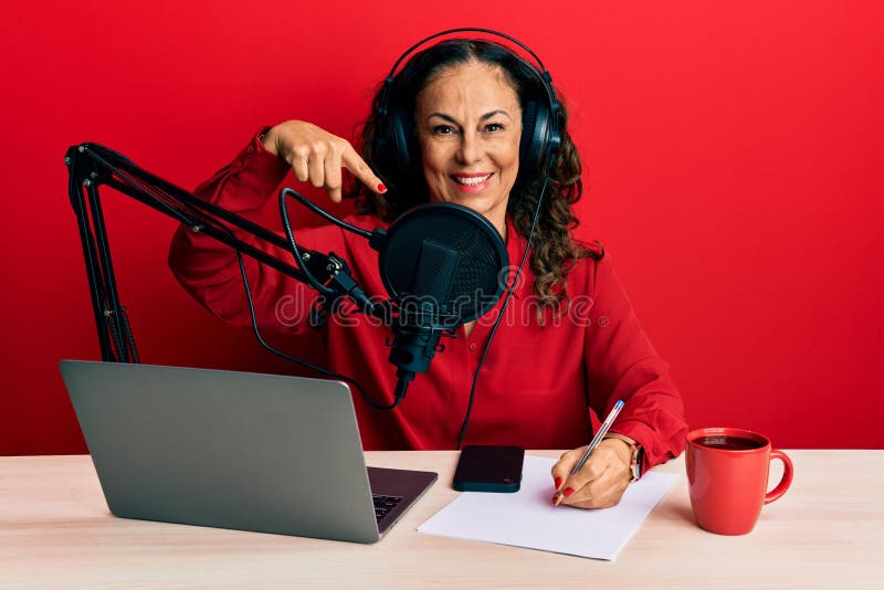 Belle femme d'âge mûr travaillant à radio studio souriant heureux pointant avec la main et le doigt