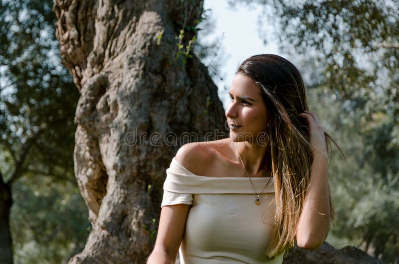 Belle femme de brune touchant ses longs cheveux Elle s'assied en parc sur l'herbe verte photo stock Belle femme de brune touchant ses longs cheveux Elle s'assied en parc sur l'herbe verte photo stock