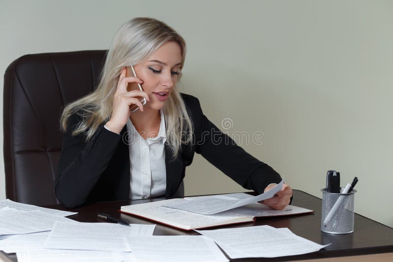 Belle femme de sourire d'affaires travaillant à son bureau avec des documents et parlant au téléphone photo stock Belle femme de sourire d'affaires travaillant à son bureau avec des documents et parlant au téléphone photo stock