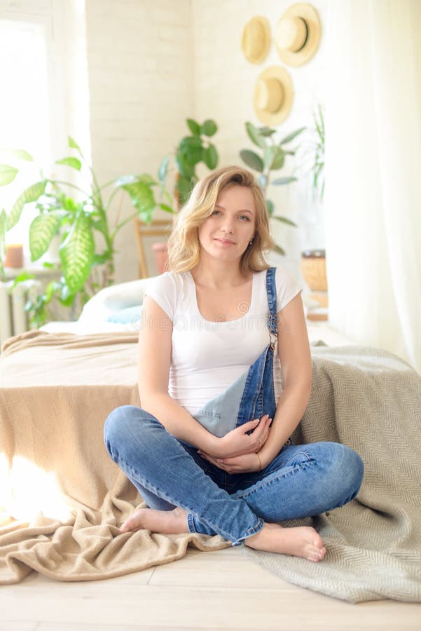 Belle femme enceinte avec les cheveux blonds dans un T-shirt blanc et des blues-jean dans une chambre avec un bon nombre de vivre photo stock Belle femme enceinte avec les cheveux blonds dans un T-shirt blanc et des blues-jean dans une chambre avec un bon nombre de vivre photo stock