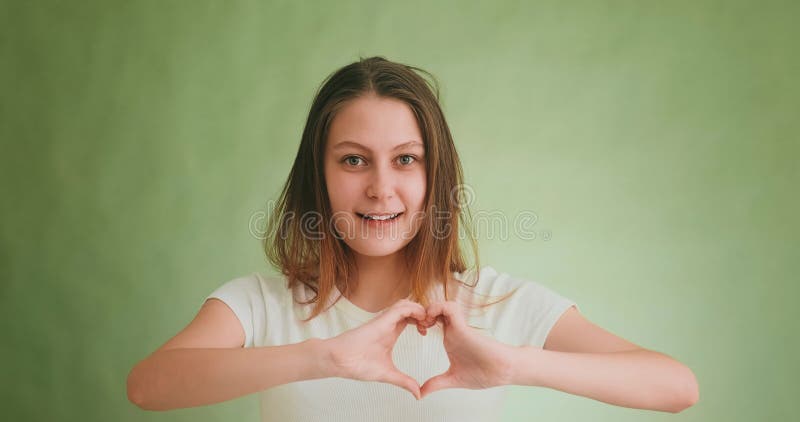 Belle femme montre coeur avec les doigts posant sur le mur vert