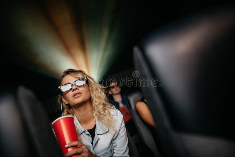 Beautiful young women with cold drink and 3d glasses watching movie in theater. Beautiful young women with cold drink and 3d glasses watching movie in theater.