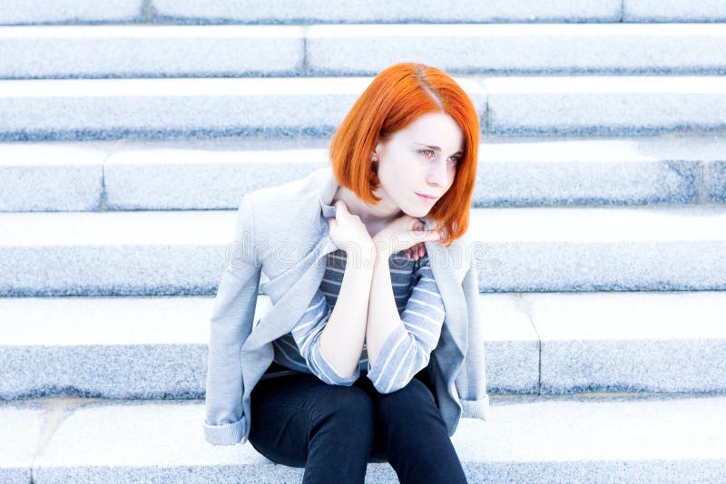 Belle femme rousse avec une veste se reposant sur les escaliers avec un regard réfléchi photos stock Belle femme rousse avec une veste se reposant sur les escaliers avec un regard réfléchi photos stock