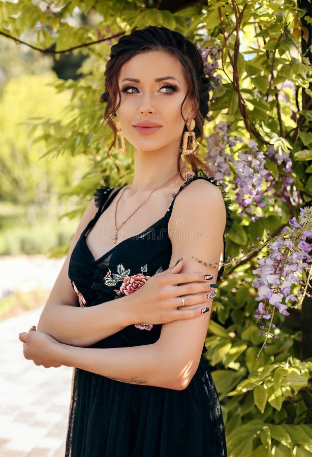 Belle femme sensuelle avec les cheveux foncés dans des vêtements élégants posant dans le jardin avec les arbres fleurissants de g photo stock Belle femme sensuelle avec les cheveux foncés dans des vêtements élégants posant dans le jardin avec les arbres fleurissants de g photo stock