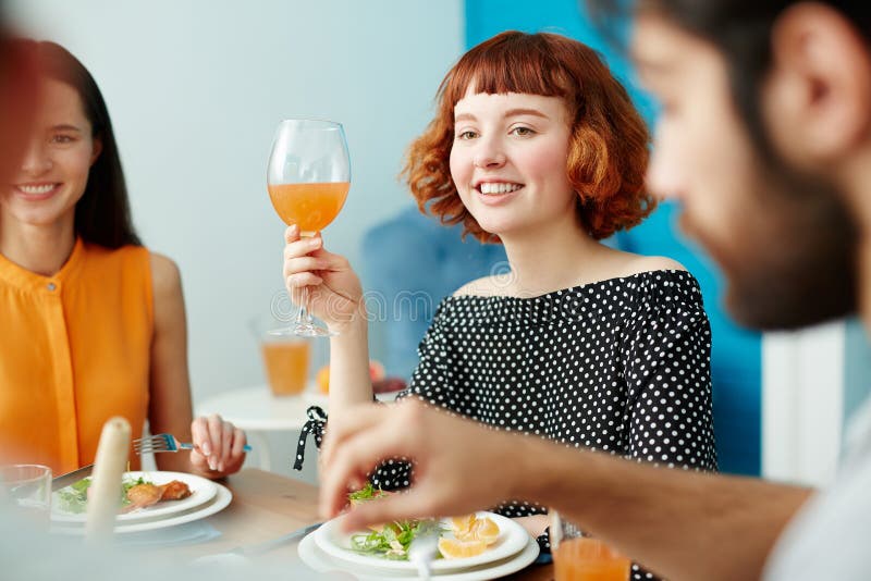 Belle femme tenant le verre tout en mangeant avec des amis photographie stock libre de droits Belle femme tenant le verre tout en mangeant avec des amis photographie stock libre de droits
