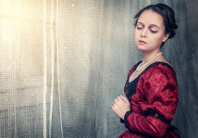 Belle femme triste dans la robe médiévale près de la fenêtre photos stock Belle femme triste dans la robe médiévale près de la fenêtre photos stock
