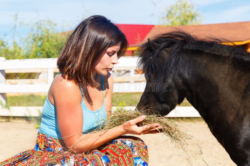 Belle fille alimentant le poney de paille à la ferme photos stock Belle fille alimentant le poney de paille à la ferme photos stock