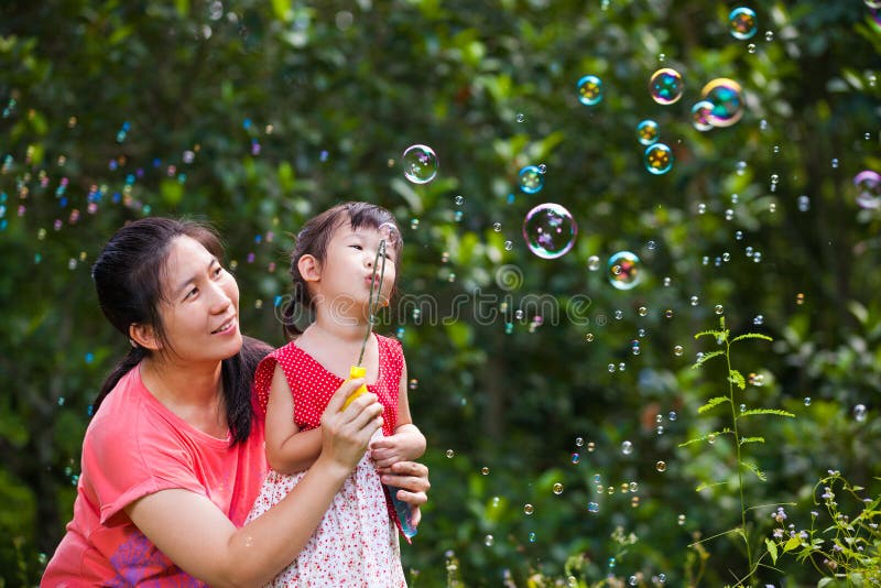 Belle fille asiatique et ses bulles de savon de soufflement de mère Famille dedans photos stock Belle fille asiatique et ses bulles de savon de soufflement de mère Famille dedans photos stock