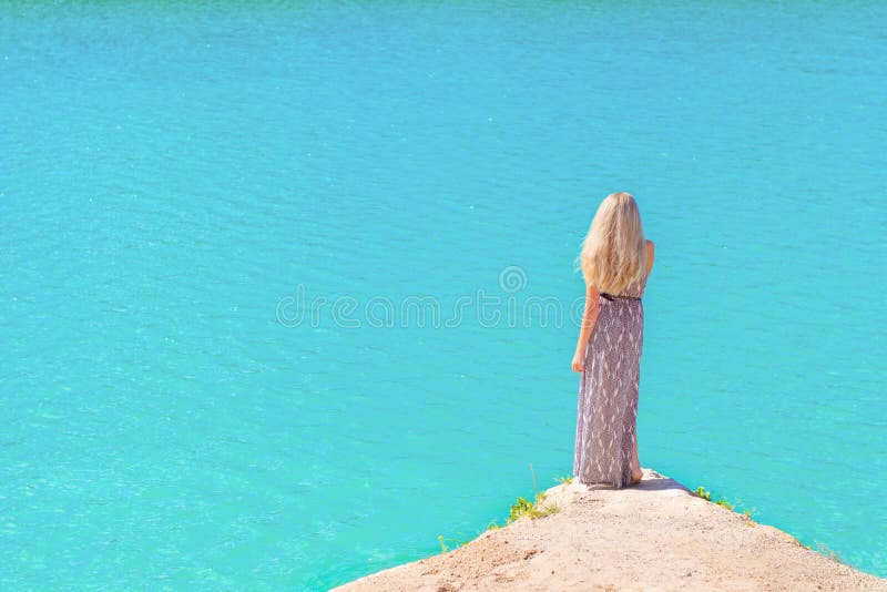 Belle fille avec de longs cheveux blancs dans une longue robe se tenant sur le rivage du lac avec de l'eau bleu dans un jour lumi photo libre de droits Belle fille avec de longs cheveux blancs dans une longue robe se tenant sur le rivage du lac avec de l'eau bleu dans un jour lumi photo libre de droits