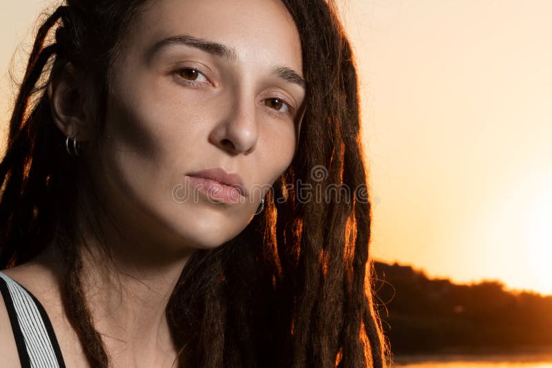 Belle fille avec des dreadlocks sans maquillage sur le fleuve dans le coucher de soleil images libres de droits