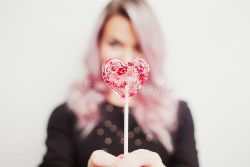 Belle fille avec du charme avec une lucette sous forme de coeur Portrait d'une jeune femme avec les cheveux roses et la sucrerie photographie stock libre de droits Belle fille avec du charme avec une lucette sous forme de coeur Portrait d'une jeune femme avec les cheveux roses et la sucrerie photographie stock libre de droits
