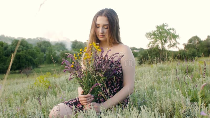 Belle fille avec le bouquet de fleurs sauvages sur la jeune femme de pré avec de longs cheveux dans la robe en marchant sur la nat banque de vidéos