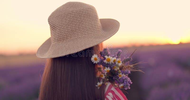 Belle fille avec robe d'été et chapeau dans un champ de lavande violet regardez coucher de soleil scénique à l'horizon clips vidéos