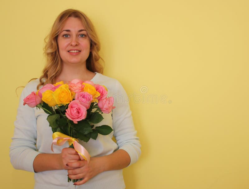Belle fille blonde dans le bouquet bleu de participation de robe des roses jaunes et roses sur un fond jaune-clair photographie stock libre de droits Belle fille blonde dans le bouquet bleu de participation de robe des roses jaunes et roses sur un fond jaune-clair photographie stock libre de droits