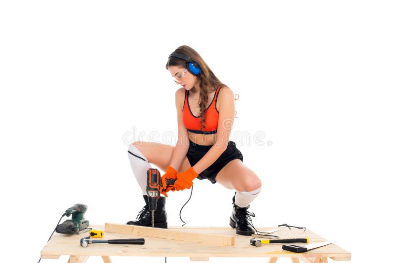 belle fille dans des écouteurs protecteurs fonctionnant avec le foret électrique à la table en bois avec des outils, images stock belle fille dans des écouteurs protecteurs fonctionnant avec le foret électrique à la table en bois avec des outils, images stock