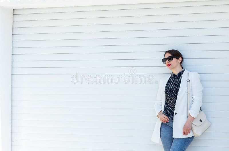 Belle fille dans la veste et des jeans blancs au fond blanc de mur de porte de garage Été occasionnel à la mode d'équipement de m images stock Belle fille dans la veste et des jeans blancs au fond blanc de mur de porte de garage Été occasionnel à la mode d'équipement de m images stock