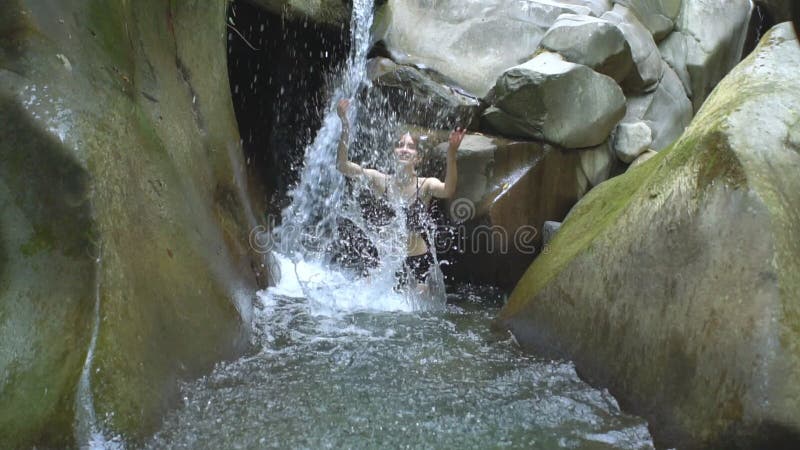 Belle fille dans le mouvement lent éclaboussant l'eau claire du lac et des regards de montagne à la caméra de la petite cascade e