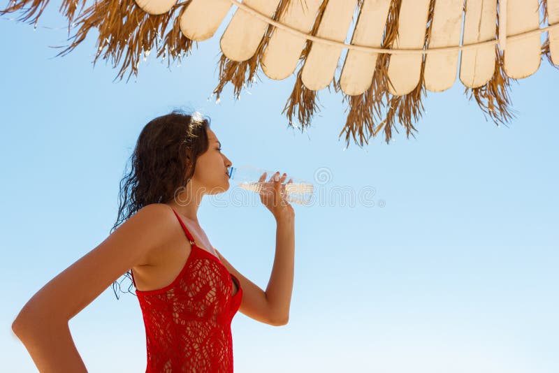Belle fille de brune en eau potable de maillot de bain rouge un jour de vacances photos stock Belle fille de brune en eau potable de maillot de bain rouge un jour de vacances photos stock