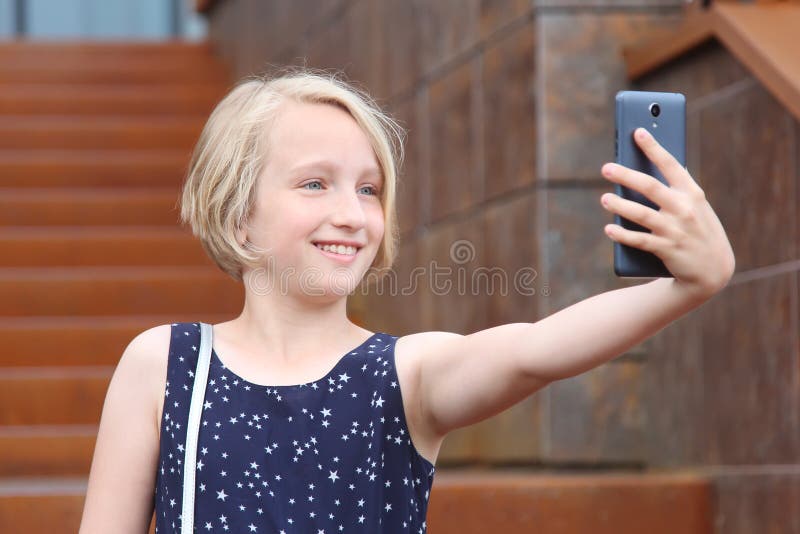 Belle fille de la préadolescence blonde à l'aide d'un téléphone, prenant un autoportrait avec le téléphone portable photo stock