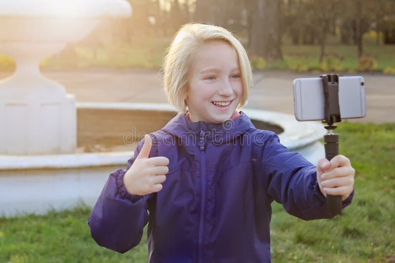 Belle fille de la préadolescence de sourire 9-11 ans prenant un selfie dehors Enfant prenant un autoportrait avec le téléphone po image stock