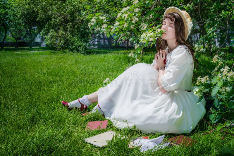 Belle fille en robe blanche est assise sur une pelouse dans un parc photos stock