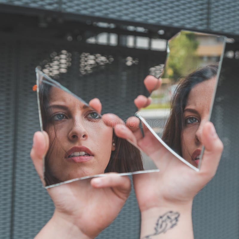 Belle fille regardant elle-même dans un miroir cassé photographie stock Belle fille regardant elle-même dans un miroir cassé photographie stock
