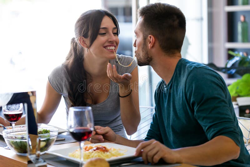 Belle giovani coppie che dividono i singoli spaghetti che ottengono più vicino a baciare nella cucina a casa fotografia stock libera da diritti Belle giovani coppie che dividono i singoli spaghetti che ottengono più vicino a baciare nella cucina a casa fotografia stock libera da diritti