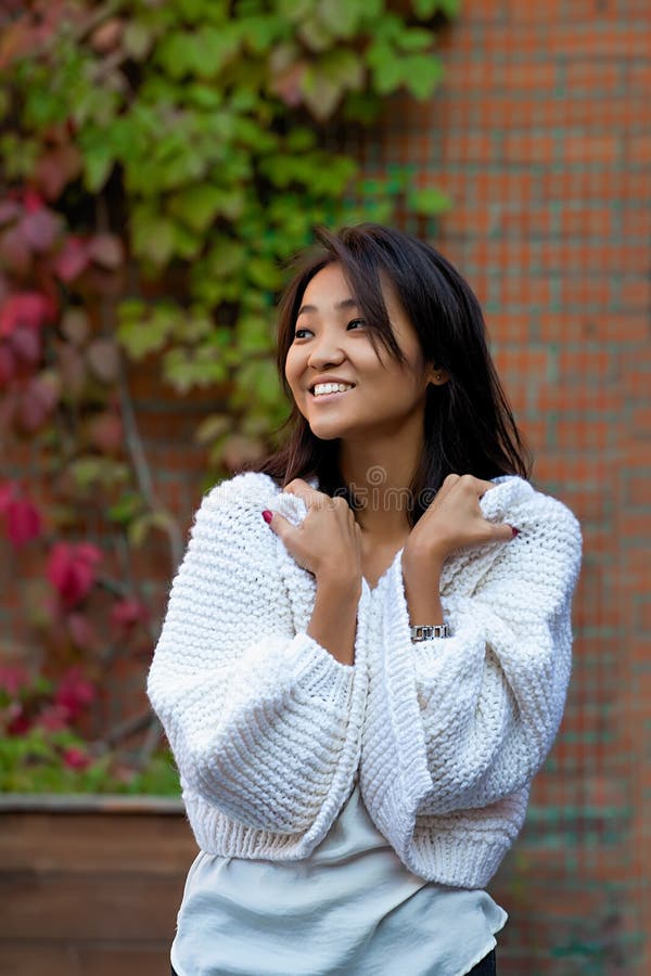 Belle jeune femme asiatique se tenant dans un cardigan chaud pourpre tricoté à côté d'un mur de briques images libres de droits Belle jeune femme asiatique se tenant dans un cardigan chaud pourpre tricoté à côté d'un mur de briques images libres de droits