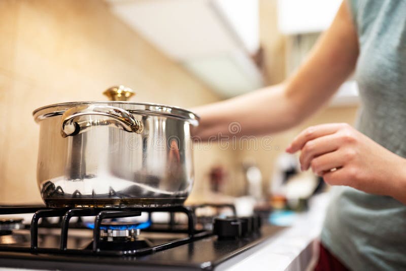Belle jeune femme au foyer qui prépare le dîner, tient-en main une grosse casserole en acier, la tenant sur un poêle à gaz photo libre de droits Belle jeune femme au foyer qui prépare le dîner, tient-en main une grosse casserole en acier, la tenant sur un poêle à gaz photo libre de droits