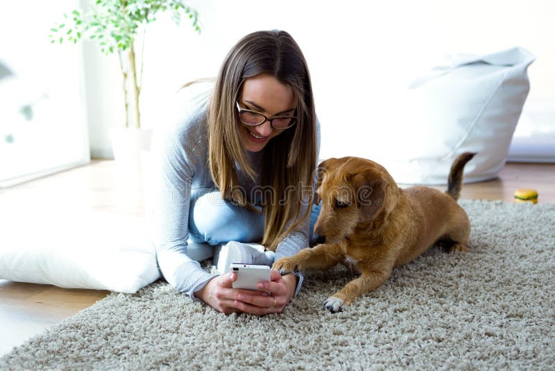Belle jeune femme avec son chien utilisant le téléphone portable à la maison