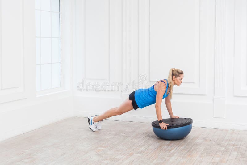 Belle jeune femme blonde sportive sportive focalisée dans des shorts noirs et le fonctionnement supérieur bleu dans le gymnase fa image stock Belle jeune femme blonde sportive sportive focalisée dans des shorts noirs et le fonctionnement supérieur bleu dans le gymnase fa image stock