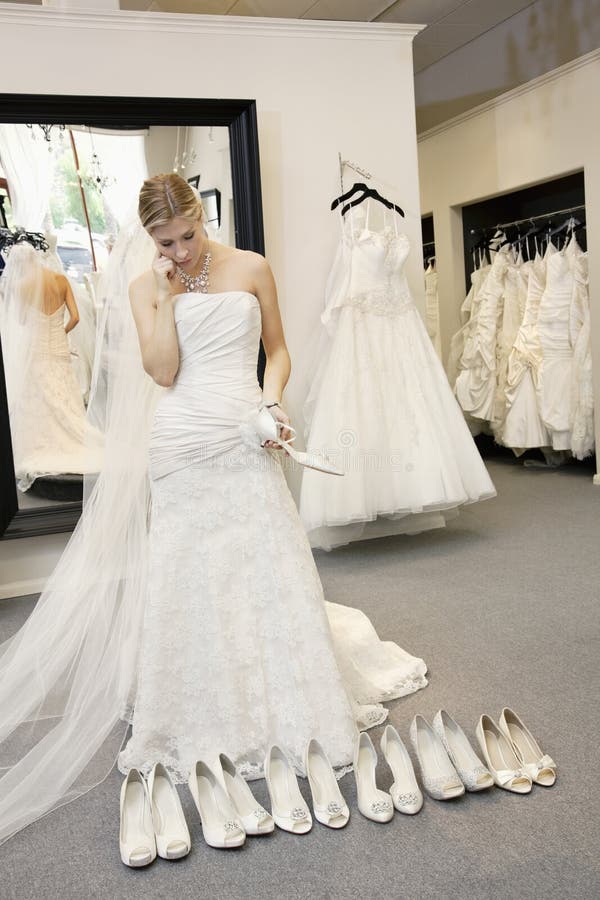 Belle jeune femme confuse tout en sélectionnant des chaussures dans la boutique nuptiale photo stock Belle jeune femme confuse tout en sélectionnant des chaussures dans la boutique nuptiale photo stock