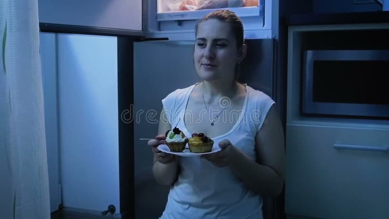 Belle jeune femme dans des pyjamas mangeant sur la cuisine la nuit