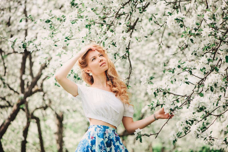 Belle jeune femme dans la maxi jupe florale marchant dans le jardin de floraison de ressort photographie stock Belle jeune femme dans la maxi jupe florale marchant dans le jardin de floraison de ressort photographie stock
