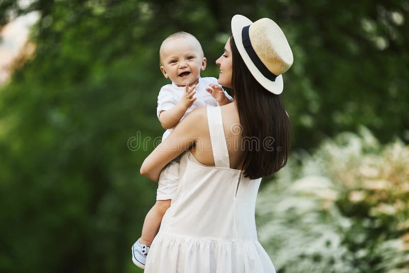 Belle jeune femme dans le chapeau élégant et dans une robe blanche avec son petit fils mignon dans la chemise et des shorts sur s photo stock Belle jeune femme dans le chapeau élégant et dans une robe blanche avec son petit fils mignon dans la chemise et des shorts sur s photo stock