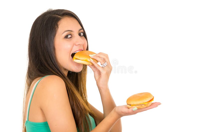 Belle jeune femme posant pour l'appareil-photo mangeant l'hamburger tout en tenant un autre dans l'autre main, souriant heureusem photos stock Belle jeune femme posant pour l'appareil-photo mangeant l'hamburger tout en tenant un autre dans l'autre main, souriant heureusem photos stock