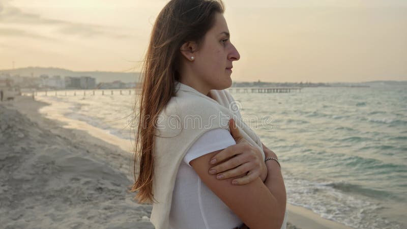 Belle jeune femme regardant le coucher du soleil sur la plage de mer par temps froid