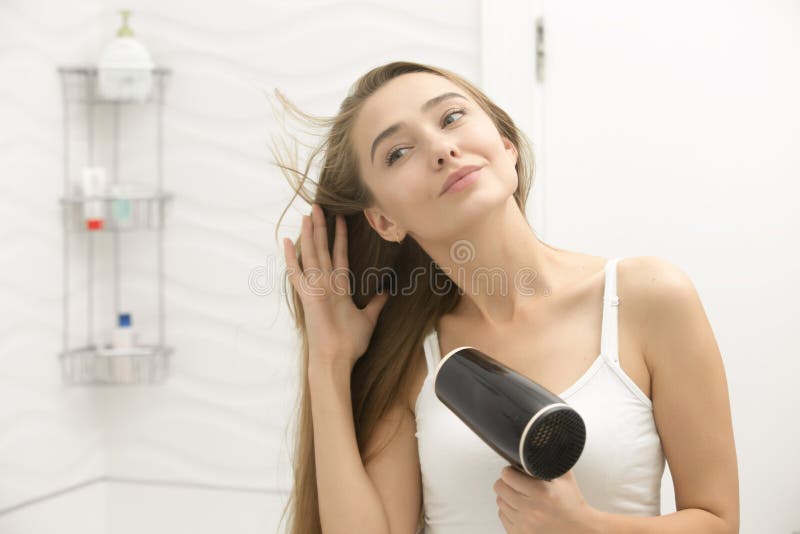 Belle jeune femme regardant les cheveux de séchage de miroir photos libres de droits Belle jeune femme regardant les cheveux de séchage de miroir photos libres de droits