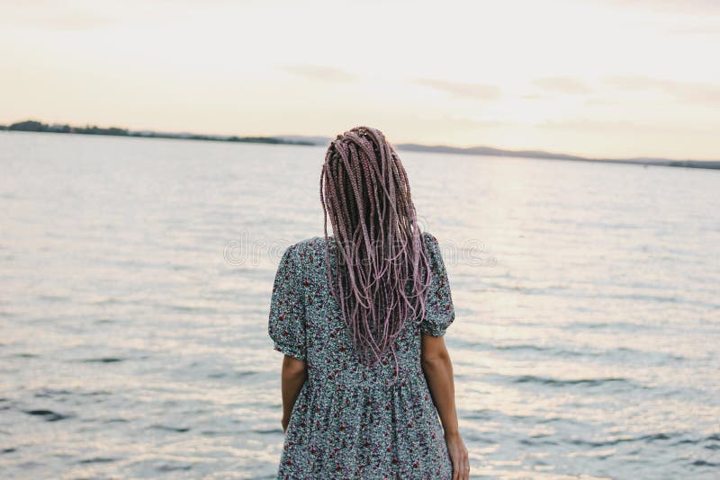 Belle jeune femme romantique avec les tresses africaines dans la robe sur la plage, vue par derrière, temps de vacances d'été image stock Belle jeune femme romantique avec les tresses africaines dans la robe sur la plage, vue par derrière, temps de vacances d'été image stock