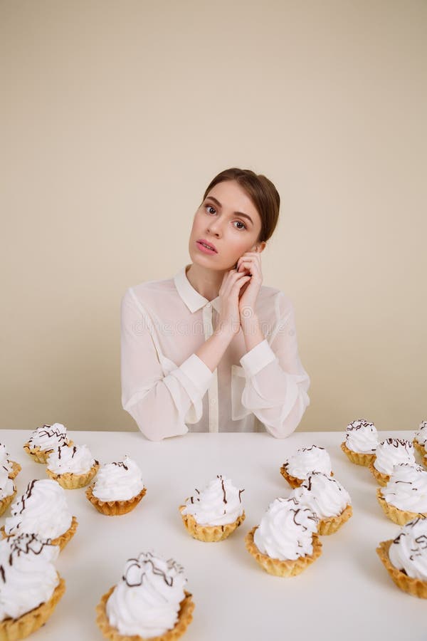 Belle jeune femme s'asseyant à la table avec des petits gâteaux images stock