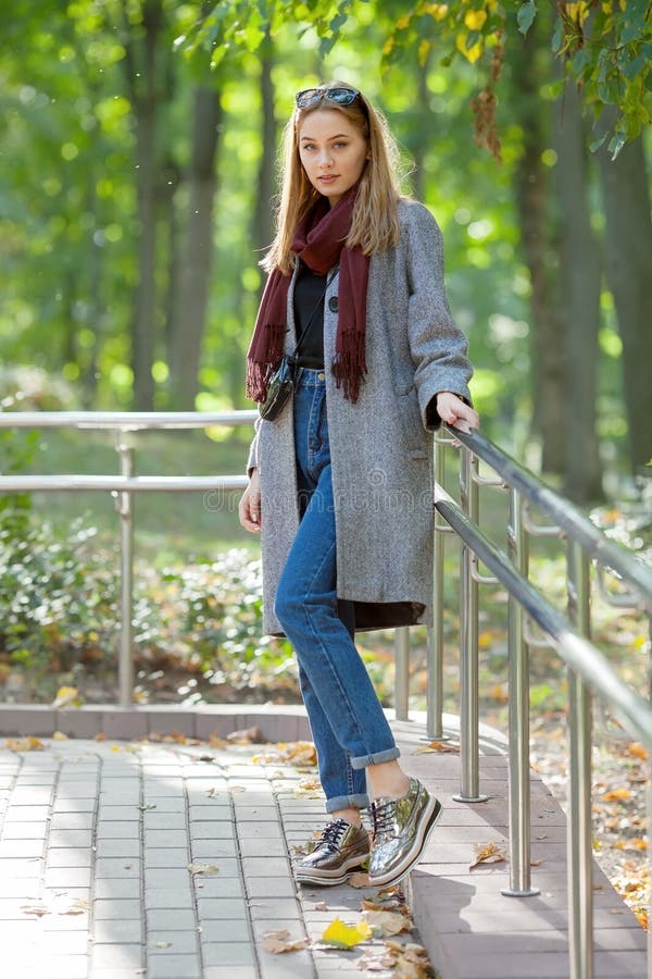 Belle jeune femme élégante dans les chaussures à la mode de blues-jean chaudes d'une écharpe et le manteau confortable marchant l photo stock Belle jeune femme élégante dans les chaussures à la mode de blues-jean chaudes d'une écharpe et le manteau confortable marchant l photo stock