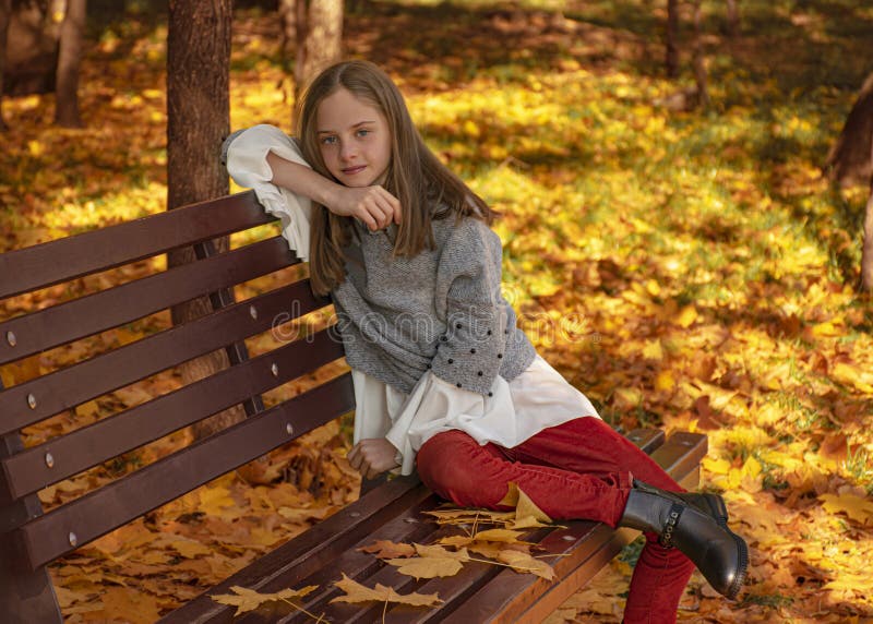 Belle jeune fille assise sur un banc de parc en bois brun à l'automne La pensée et les rêves de la femme Tombe de la feuille d'au images stock Belle jeune fille assise sur un banc de parc en bois brun à l'automne La pensée et les rêves de la femme Tombe de la feuille d'au images stock