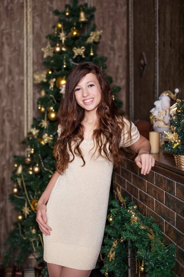 Belle jeune fille avec le sourire heureux joyeux sincère ouvert dans la rétro robe d'or de vintage tenant la cheminée et l'arbre image stock Belle jeune fille avec le sourire heureux joyeux sincère ouvert dans la rétro robe d'or de vintage tenant la cheminée et l'arbre image stock
