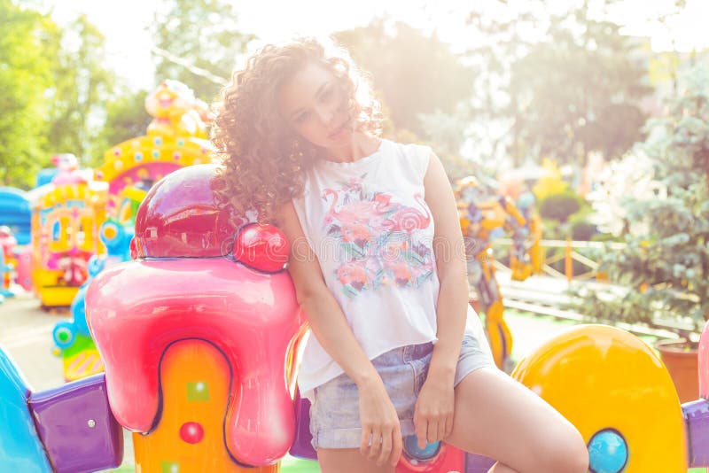 Belle jeune fille avec les cheveux bouclés dans des shorts de denim et le T-shirt blanc en parc d'attractions images stock Belle jeune fille avec les cheveux bouclés dans des shorts de denim et le T-shirt blanc en parc d'attractions images stock