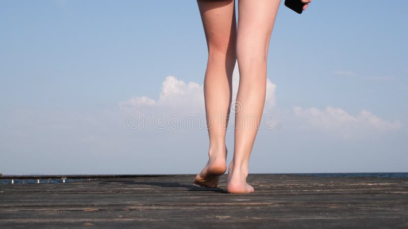 Belle jeune fille marchant sur une jetée en bois au bord de la mer. jambes se réveillant sur pont en bois fermer vidéo résolution clips vidéos