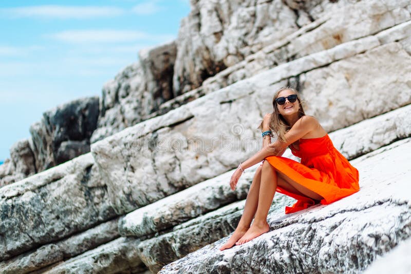 Belle jeune fille par la mer Femme dans une robe rouge sur la plage Vacances de bord de la mer Terrain rocheux photos libres de droits Belle jeune fille par la mer Femme dans une robe rouge sur la plage Vacances de bord de la mer Terrain rocheux photos libres de droits