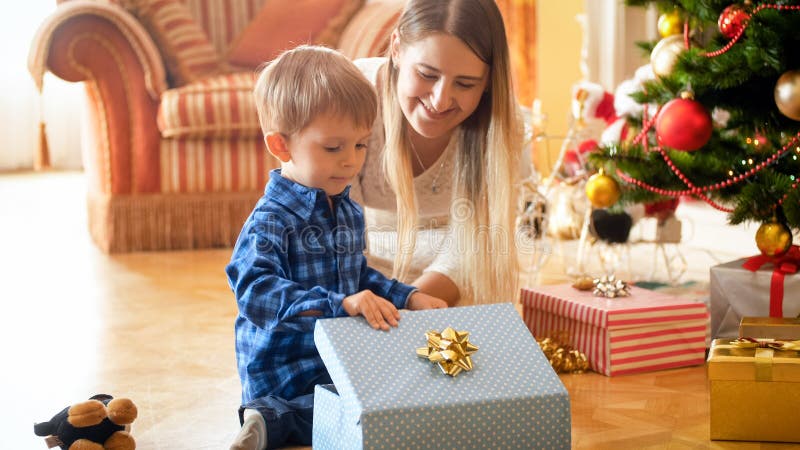 Belle mère de sourire regardant ses cadeaux et présents de Noël d'ouverture de garçon photos stock Belle mère de sourire regardant ses cadeaux et présents de Noël d'ouverture de garçon photos stock