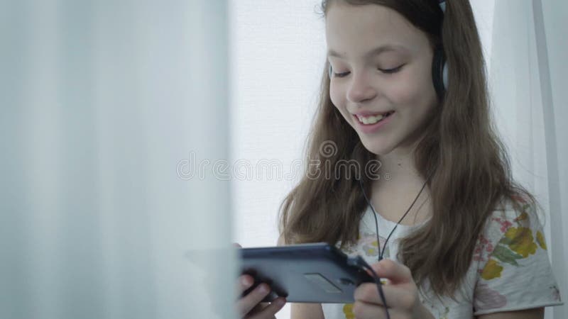 Belle petite fille avec des écouteurs observant les vidéos drôles sur le comprimé et les rires